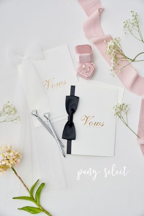 桌上擺放了婚禮誓言卡，用粉色緞帶、馬卡龍粉色的對戒戒指盒和銀色鑽石筆裝飾