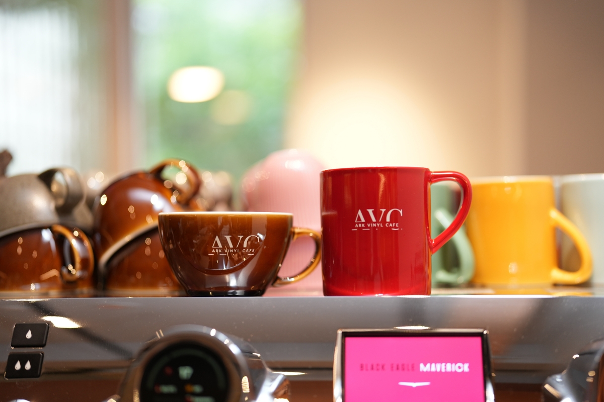 AVC Coffee Roasters 紅色馬克杯與焦糖色蛋形咖啡杯並排,杯身皆燒印白色品牌字標