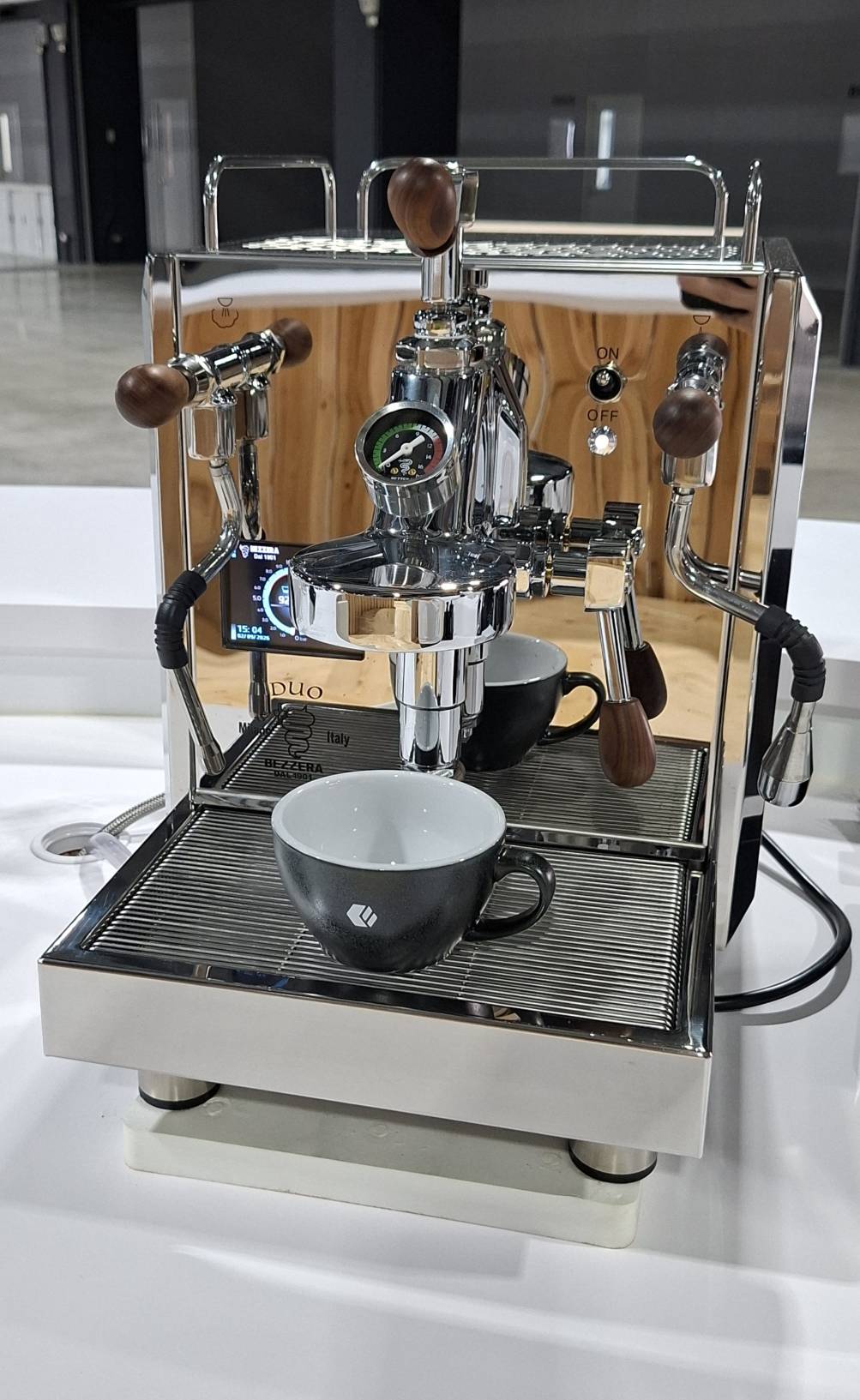 鉅鋼機械 KS KOFFEE 的咖啡機,出杯口下放著煤炭灰與黑色兩只燒印白色 Logo 的 Loveramics 蛋形咖啡杯