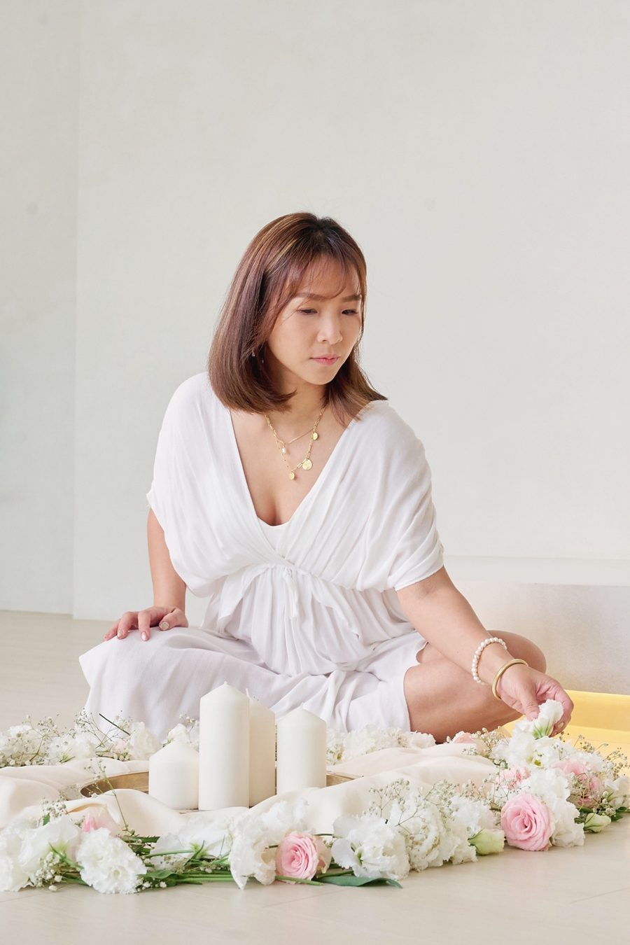 身穿白衣的 Zia 坐在花圈與燭光之間靜心