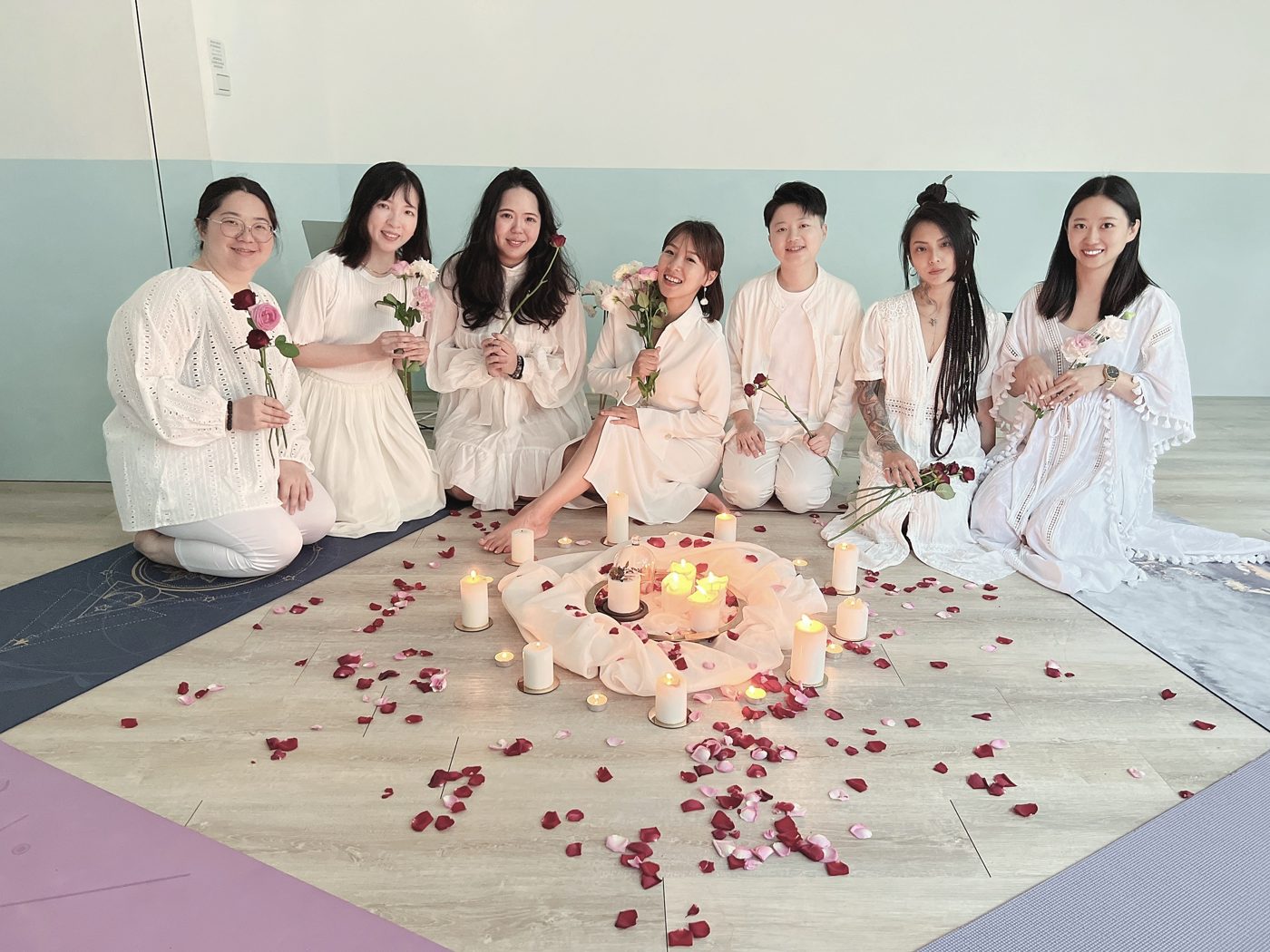 身穿白衣的學員手持玫瑰，圍坐在燭光與花瓣旁合影
