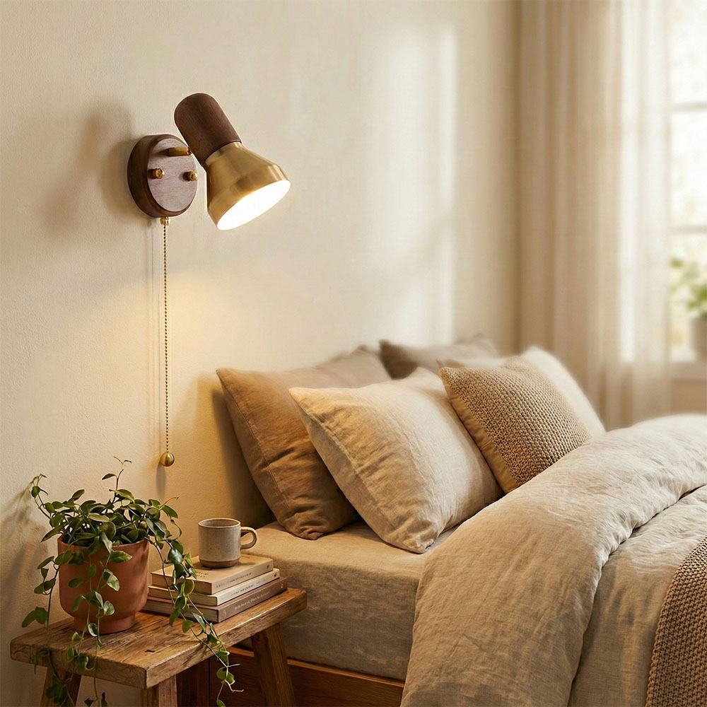 安裝於臥室米色牆面上的實木與黃銅拼接壁燈，開啟暖黃光，配有金色拉線開關，下方為木質床邊桌與綠色植栽。