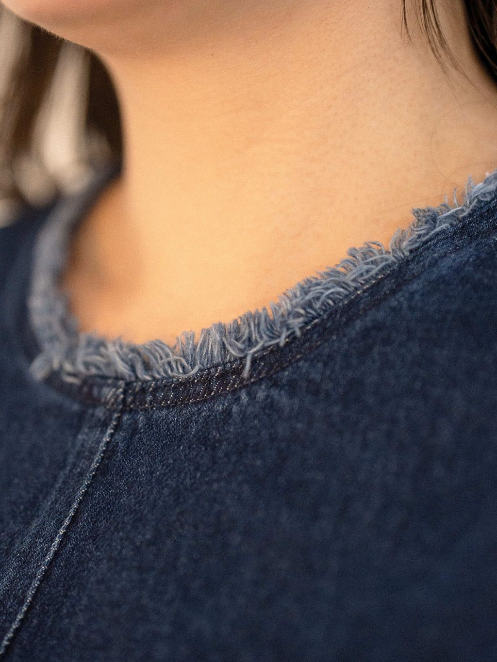Close-up of raw frayed neckline on denim top showcasing texture and craftsmanship