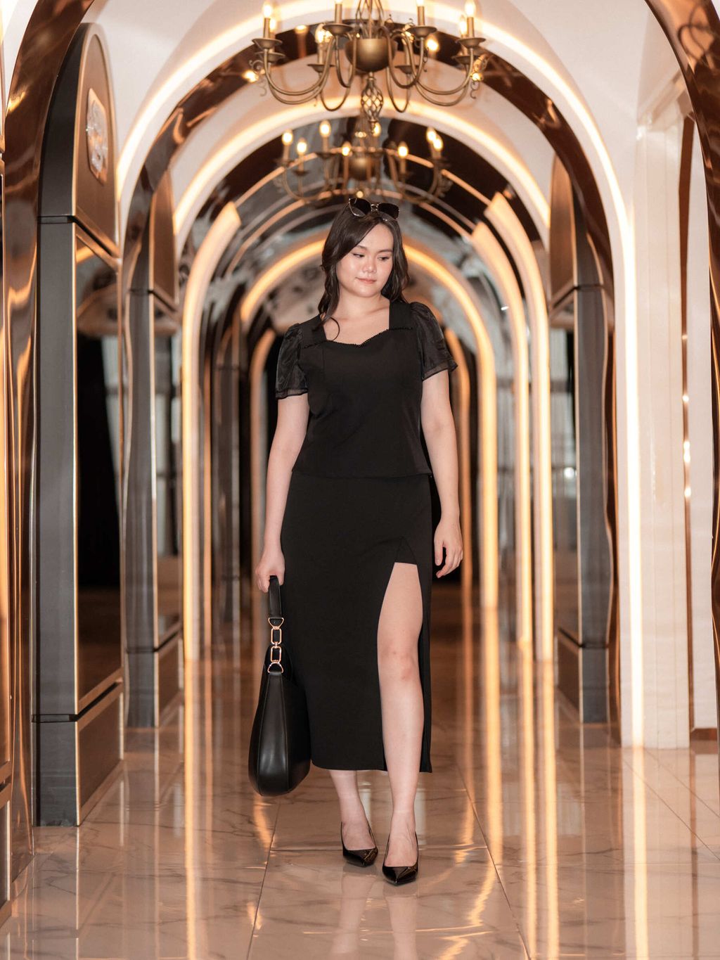 Full-length shot of a curvy woman in black plus-size outfit, striding through an elegant corridor in heels.