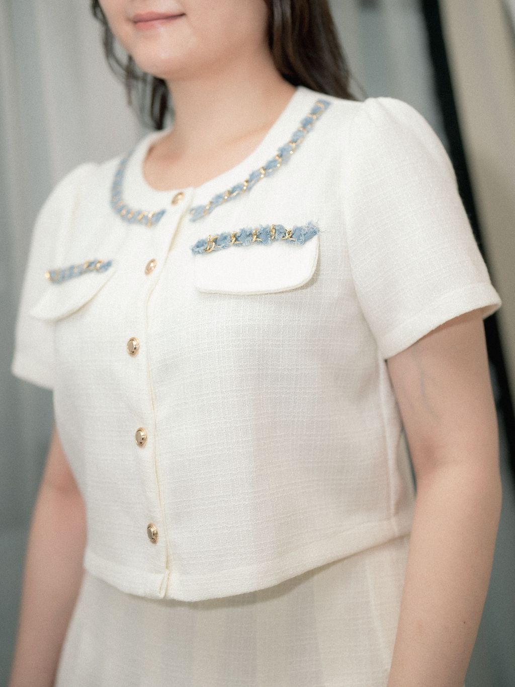 Close-up of textured white tweed fabric with pocket and button accents