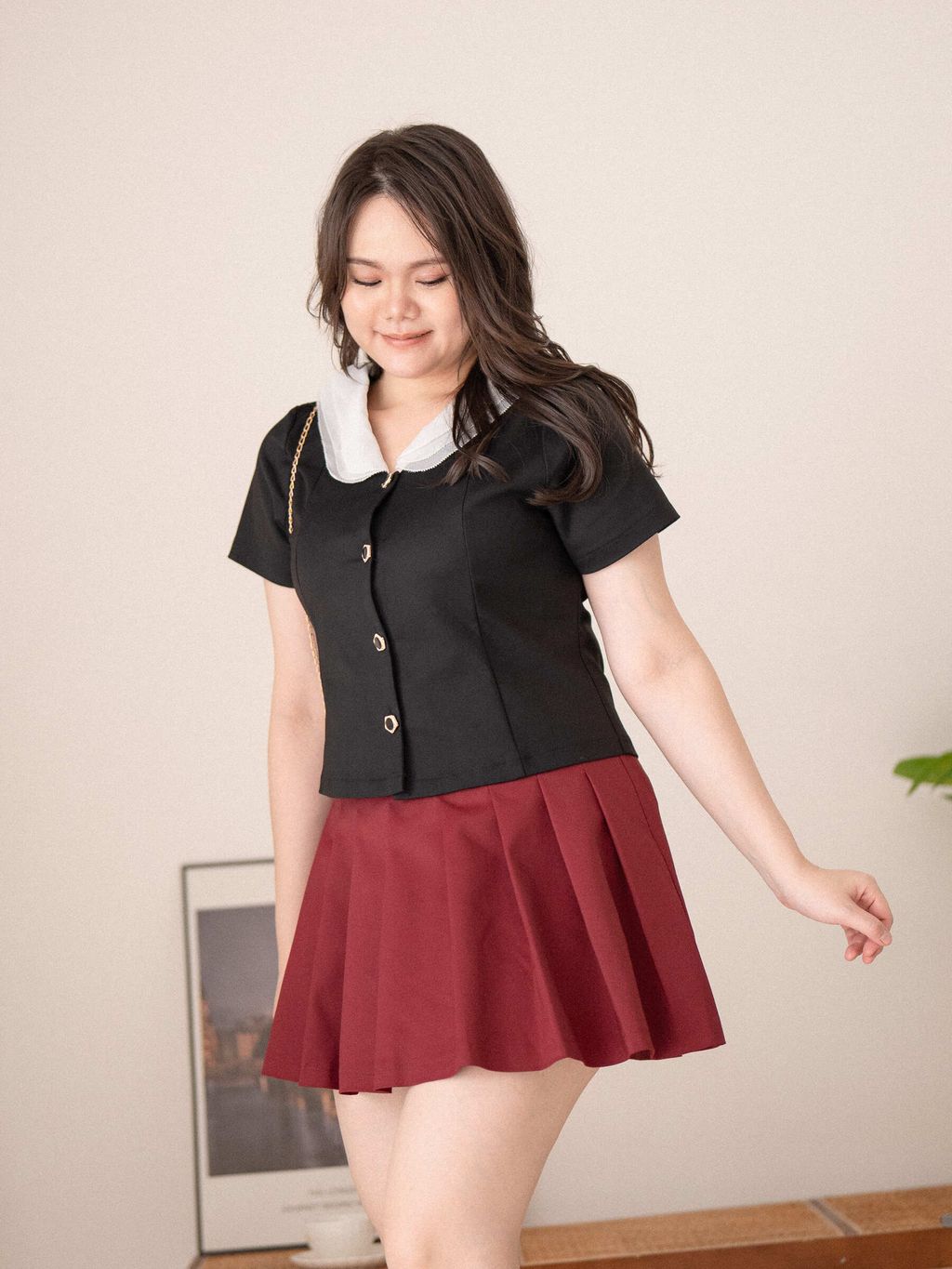 Plus-size woman in black Sweet Scholar Collar Top and maroon skirt, posing with a soft smile in a cozy room.