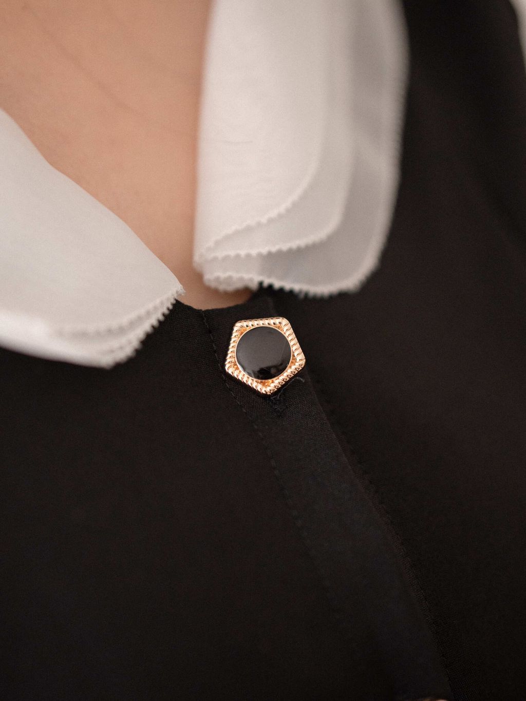 Detail shot of vintage-style gold and black button on the front of a preppy blouse.