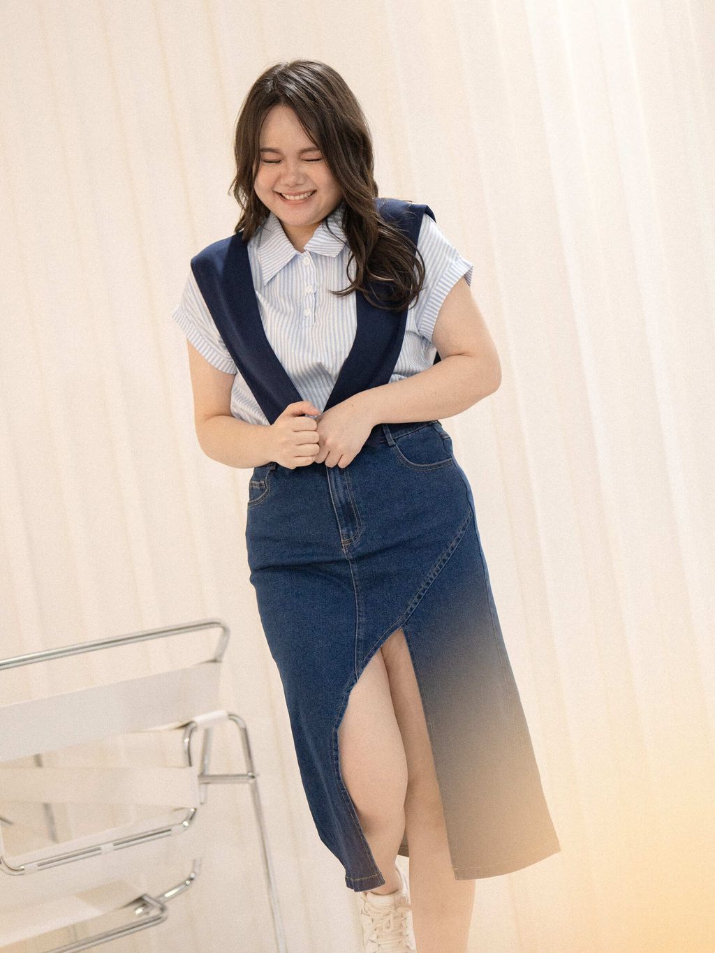 Model in plus-size denim midi skirt smiling in a bright indoor setting.