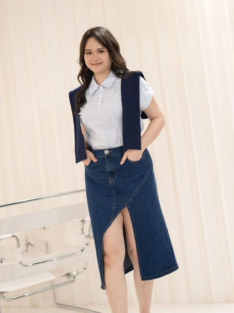 Plus-size woman wearing a dark wash denim midi skirt with an asymmetrical front slit.