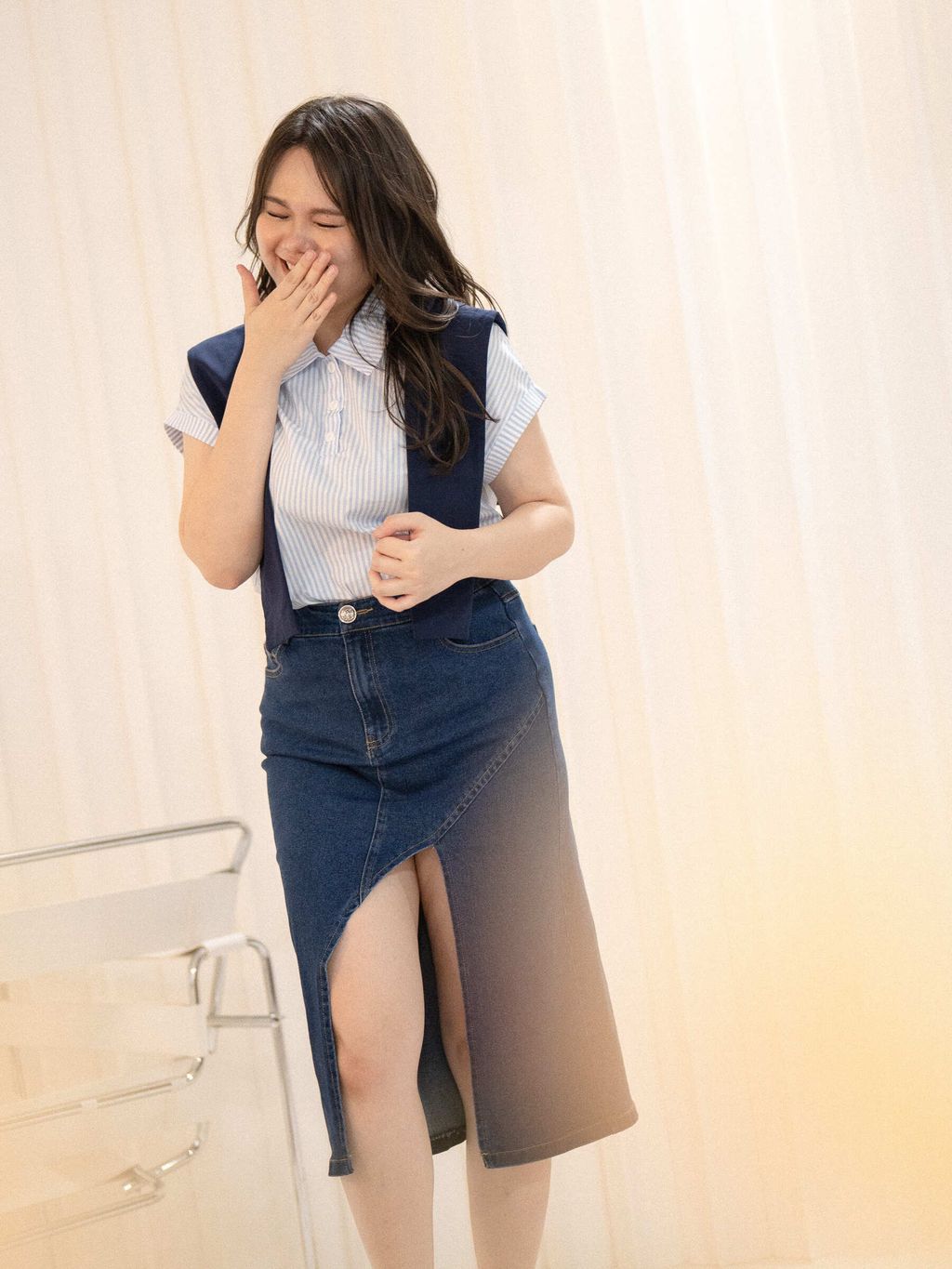 Plus-size woman smiling brightly while wearing a dark wash asymmetrical denim skirt and striped collared top.