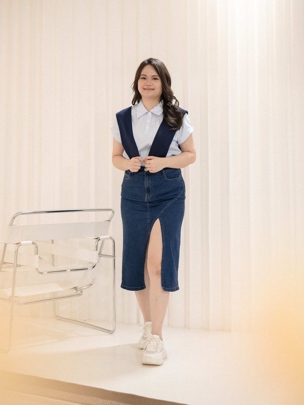 Full-body shot of asymmetrical slit denim skirt with white sneakers.