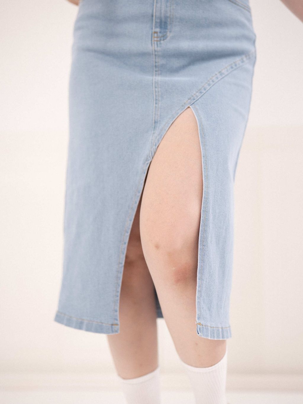 Close-up of high-waisted denim skirt with side pockets and curved seam.
