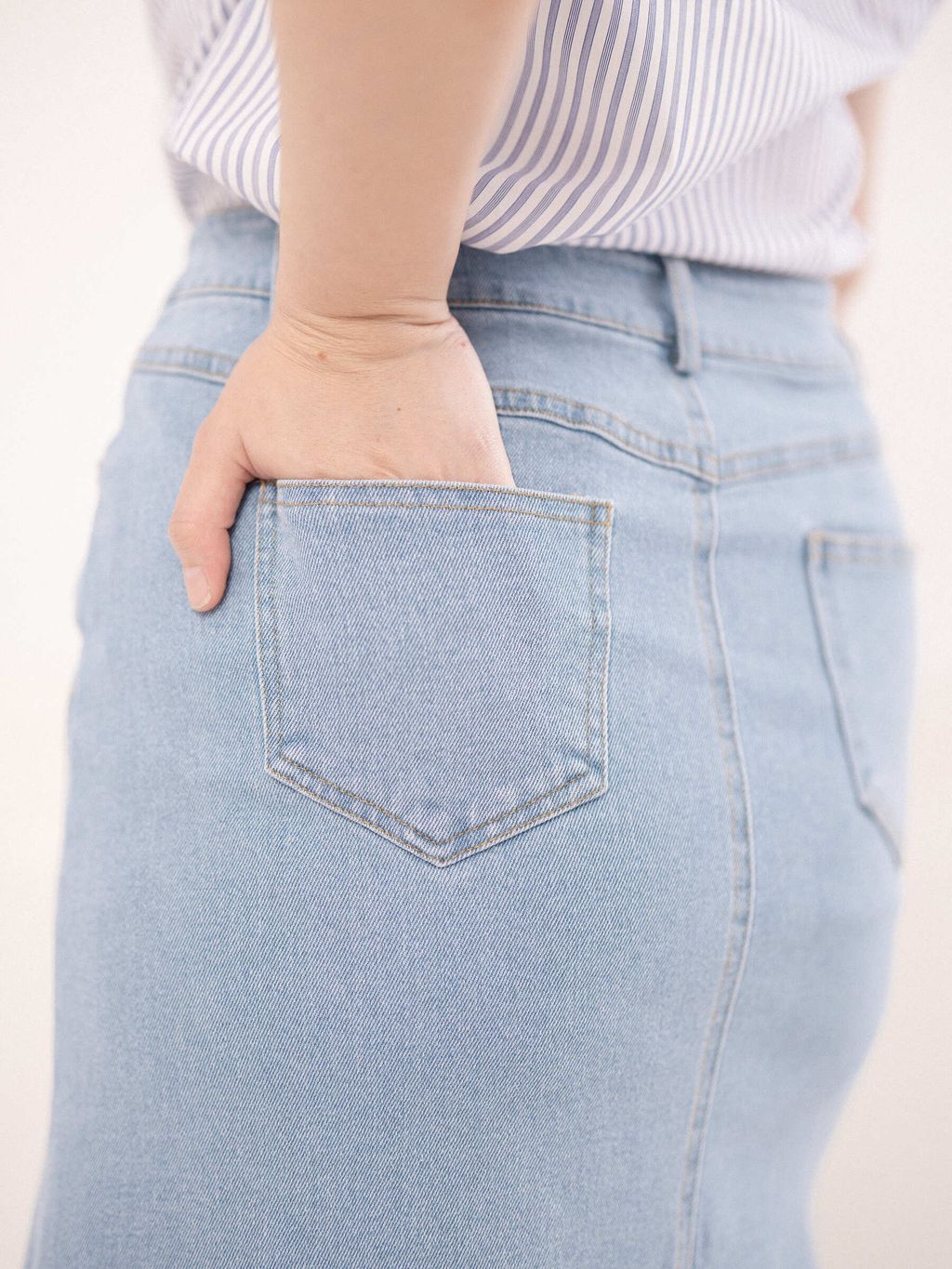 Back pocket close-up of light wash denim skirt on plus-size model.