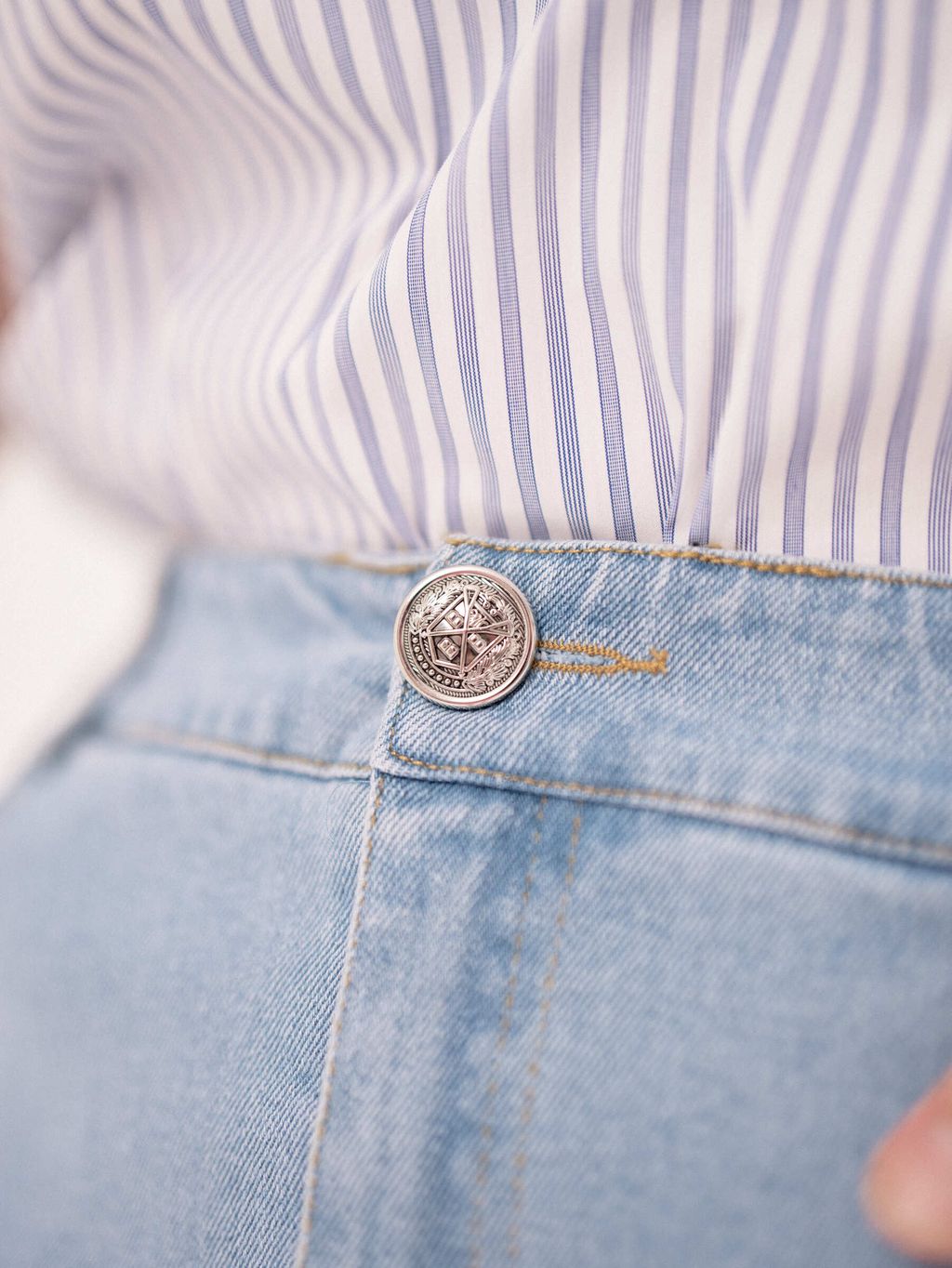 Close-up view of vintage-inspired metal button on the front of a high-waisted denim skirt.
