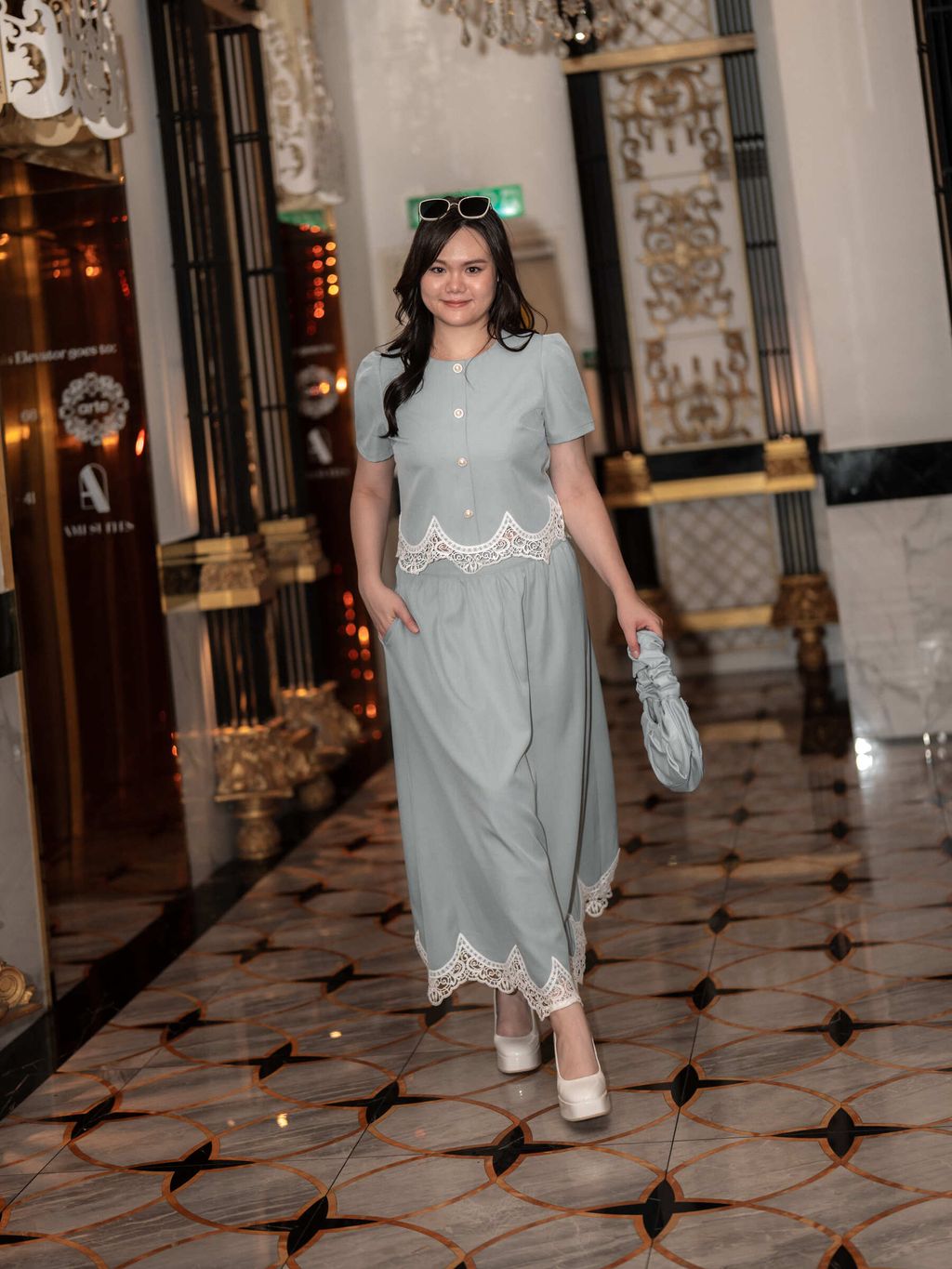 Smiling plus-size woman in scalloped lace-trimmed outfit, styled with sunglasses and a ruched handbag.