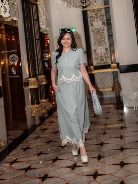 Smiling plus-size woman in scalloped lace-trimmed outfit, styled with sunglasses and a ruched handbag.