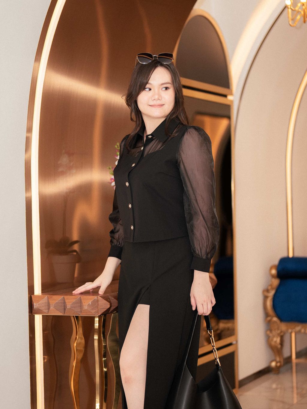 Model poses in a hallway wearing sheer sleeve blouse with midi skirt.