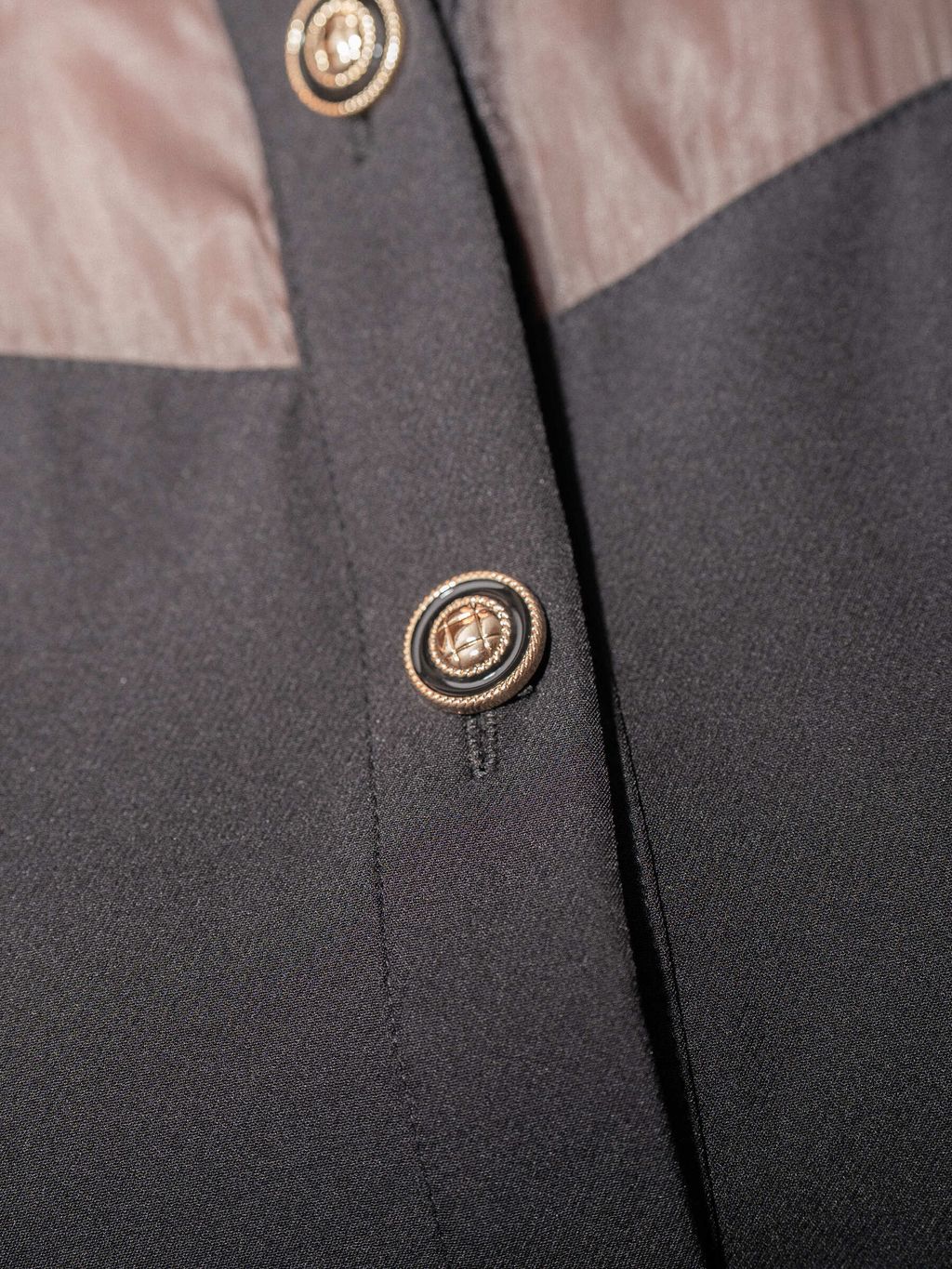 Detail close-up of gold button on a black textured blouse.