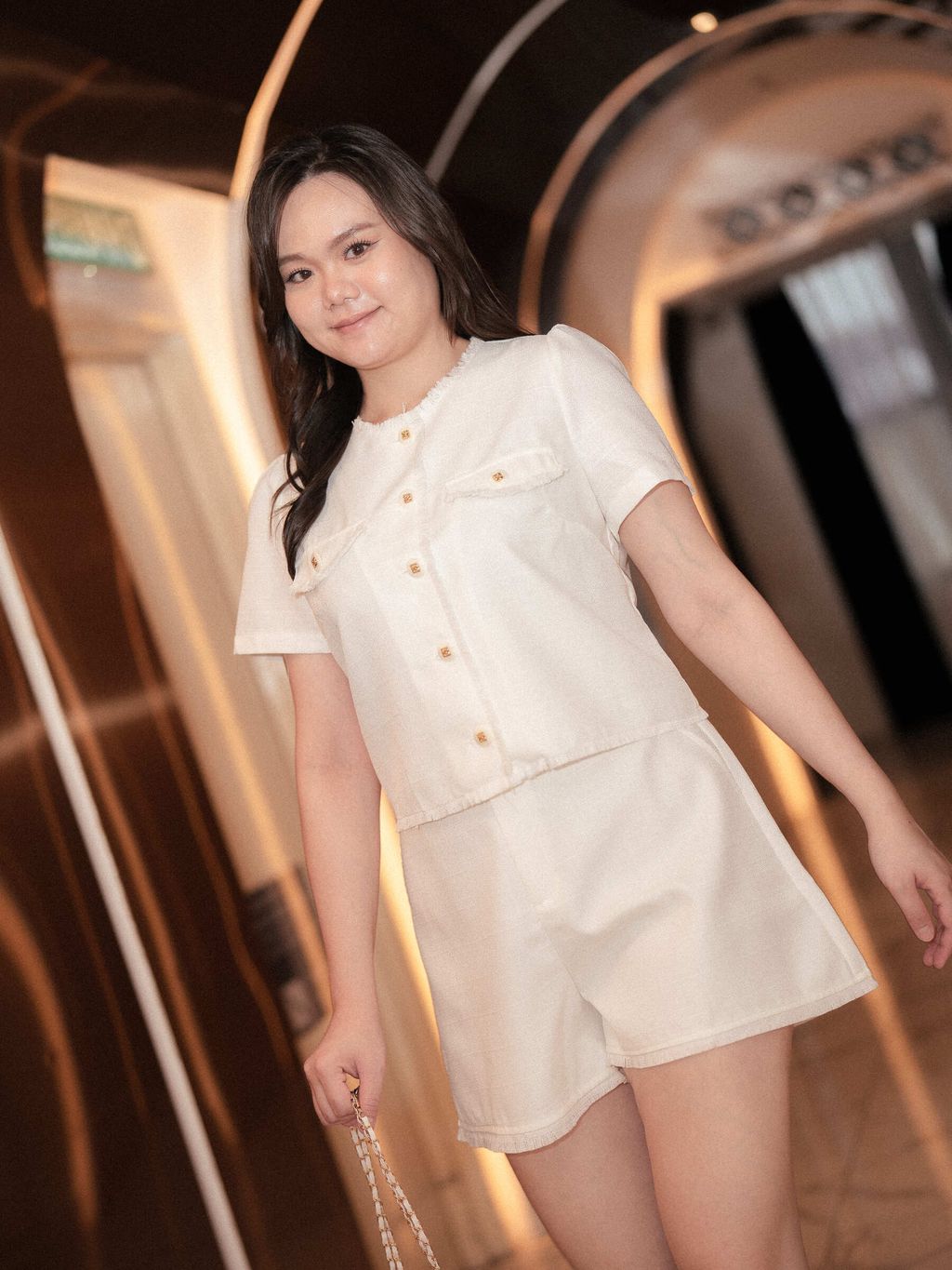 Model pairing tweed blouse with matching shorts in a hotel hallway.