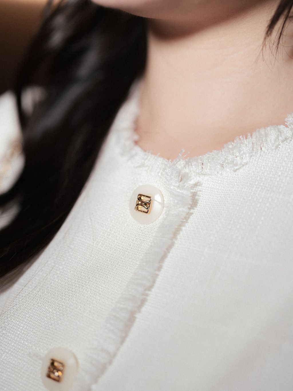 Close-up of frayed neckline and elegant front buttons on tweed blouse.