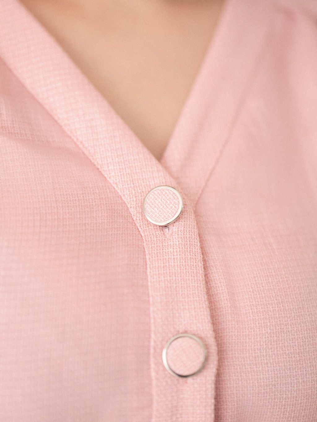 Close-up of fabric-covered round buttons on a pink textured blouse.