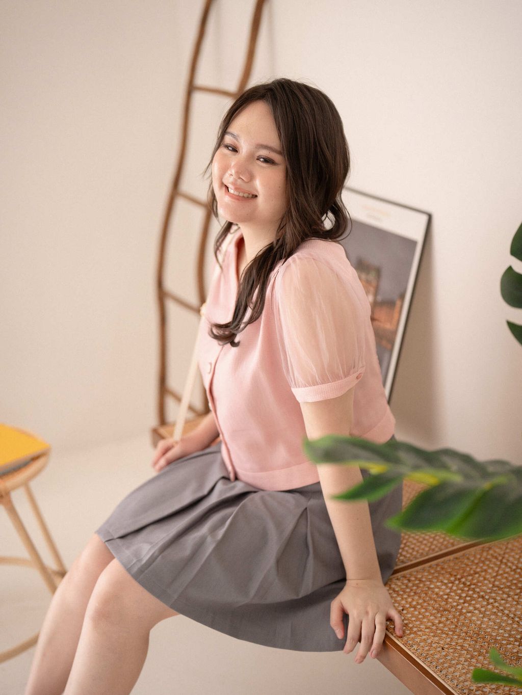 Plus-size model wearing pink textured blouse with sheer puff sleeves and grey pleated skirt.