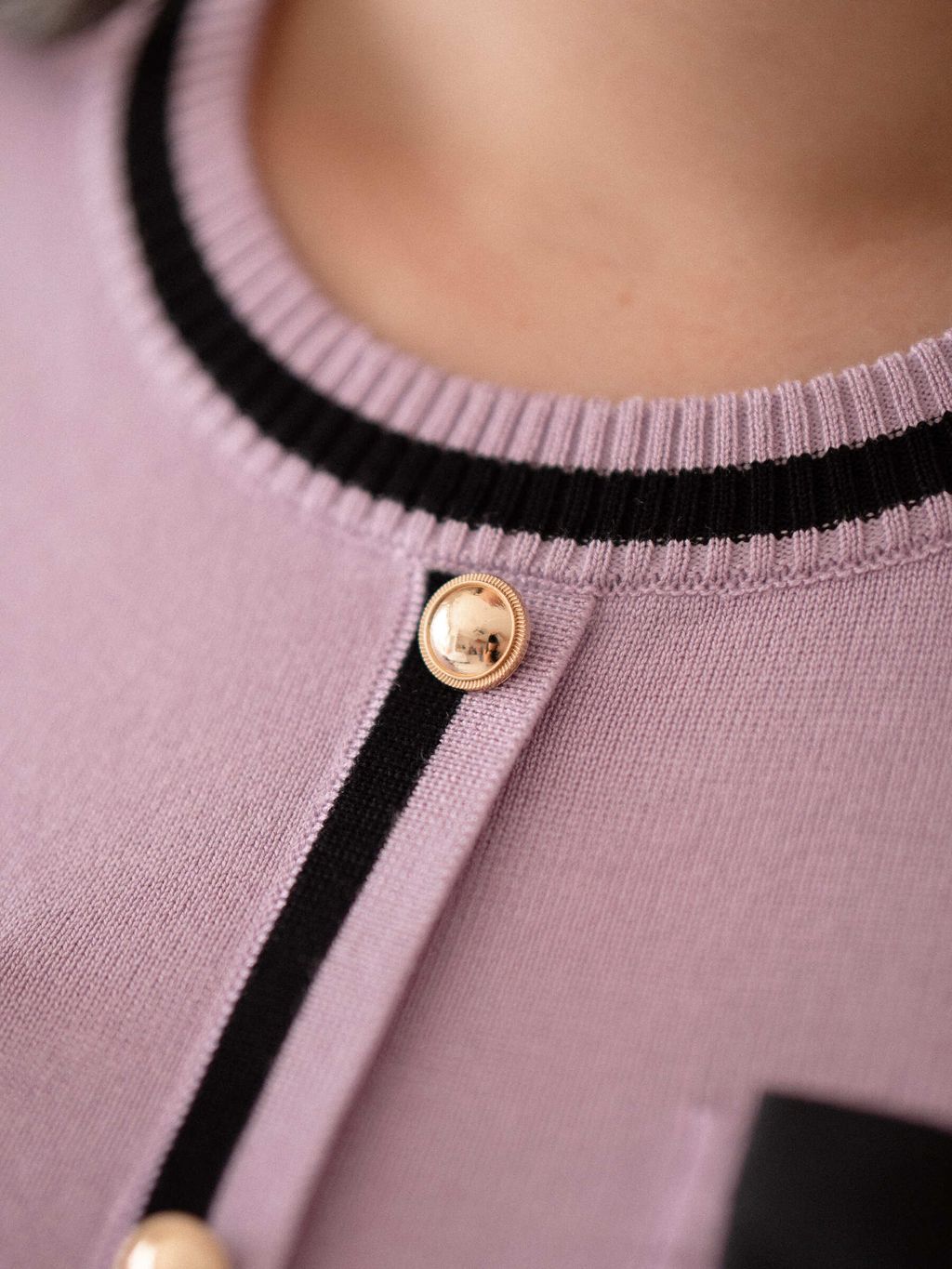 Close-up of gold button detail on lilac ribbon knit top with contrast trim.
