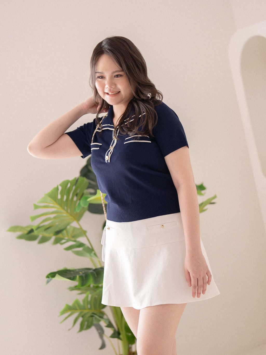 Plus-size woman wearing dark blue knit polo top with white contrast trim and gold buttons, paired with a white flared skirt for a fresh, elegant look.