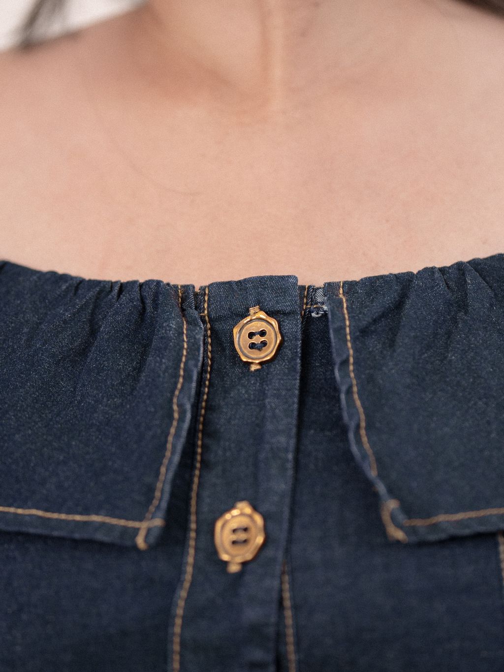 Close-up of gold-tone buttons and structured stitching on dark blue denim top.