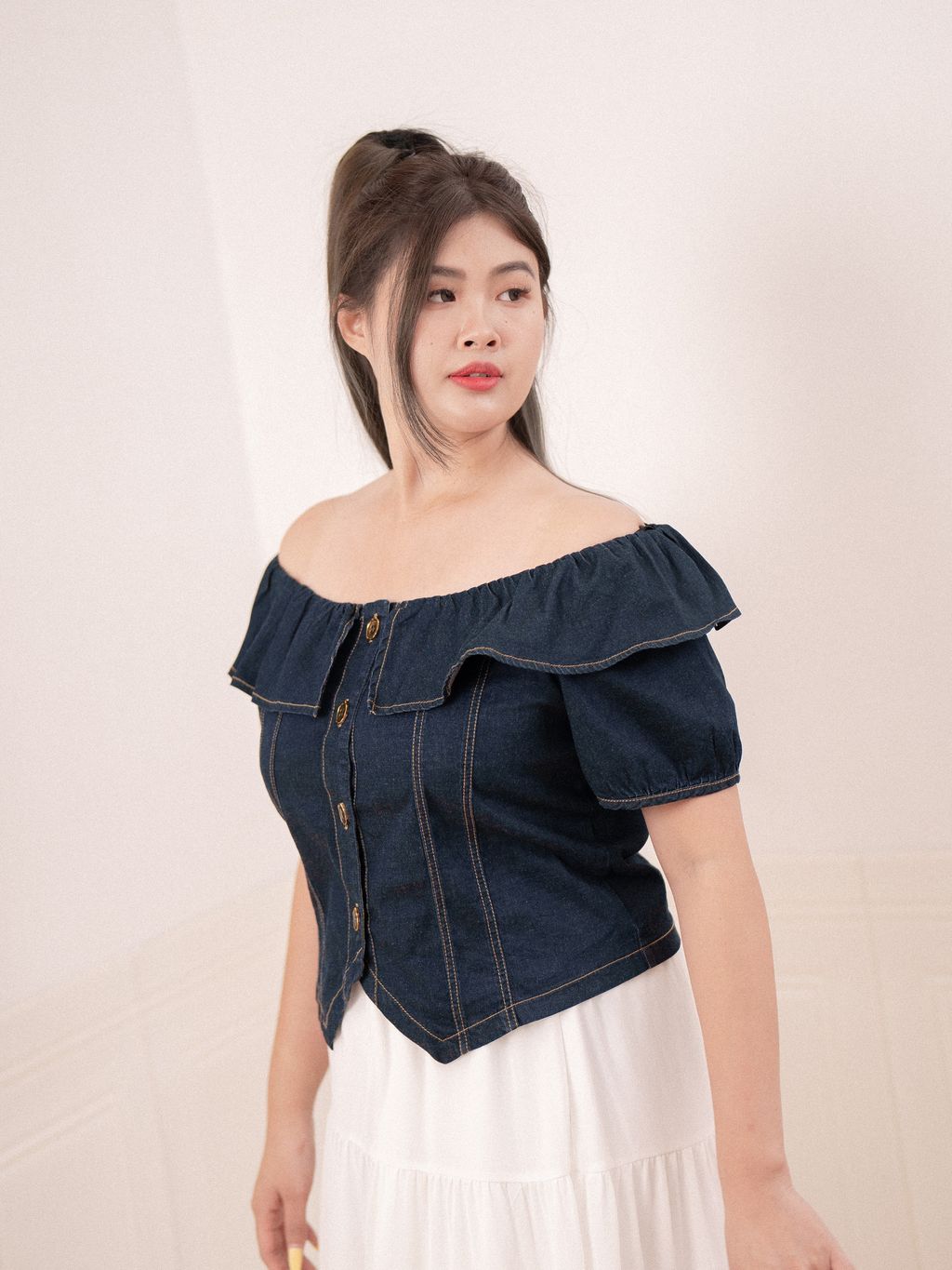 Plus-size model wearing an off-shoulder denim blouse with ruffle trim and puff sleeves.