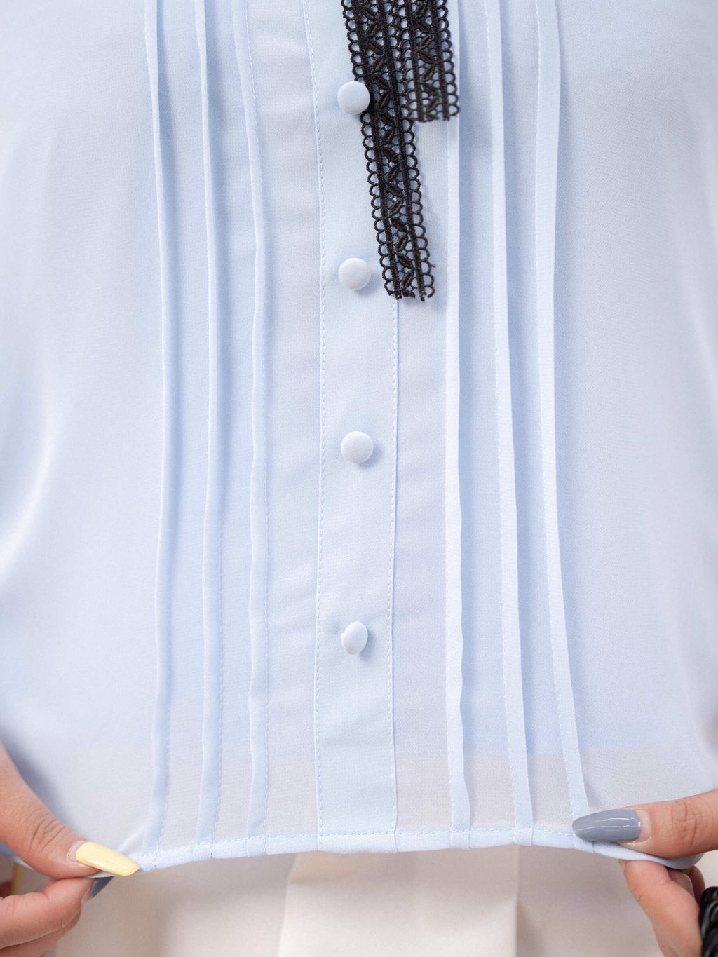 Close-up of pleated details and covered buttons on blue blouse