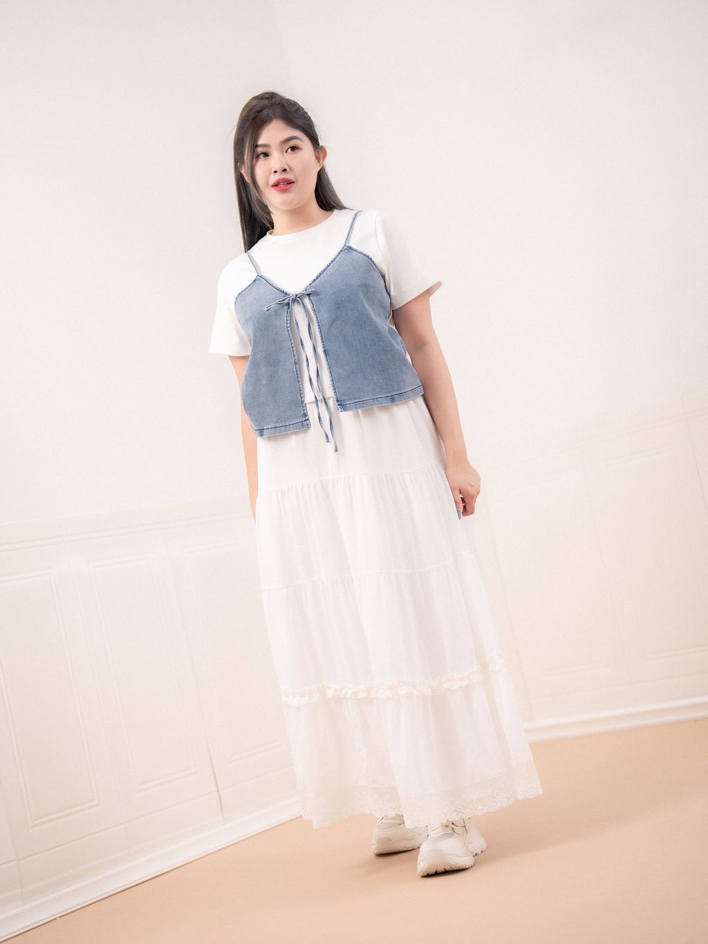 Plus-size model wearing denim tie vest layered over a white dress