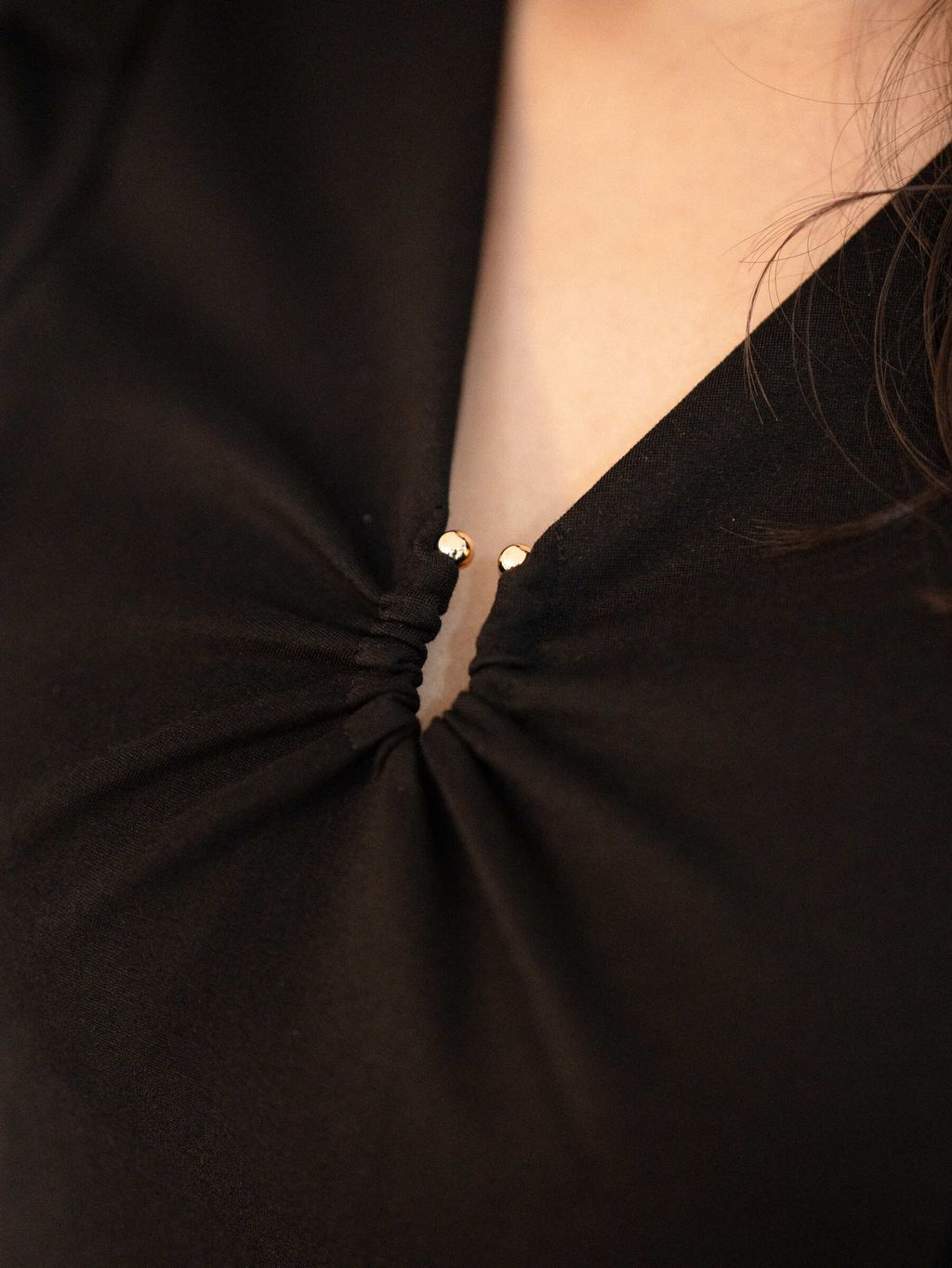 Detailed view of gathered V-neckline with gold accents on black dress