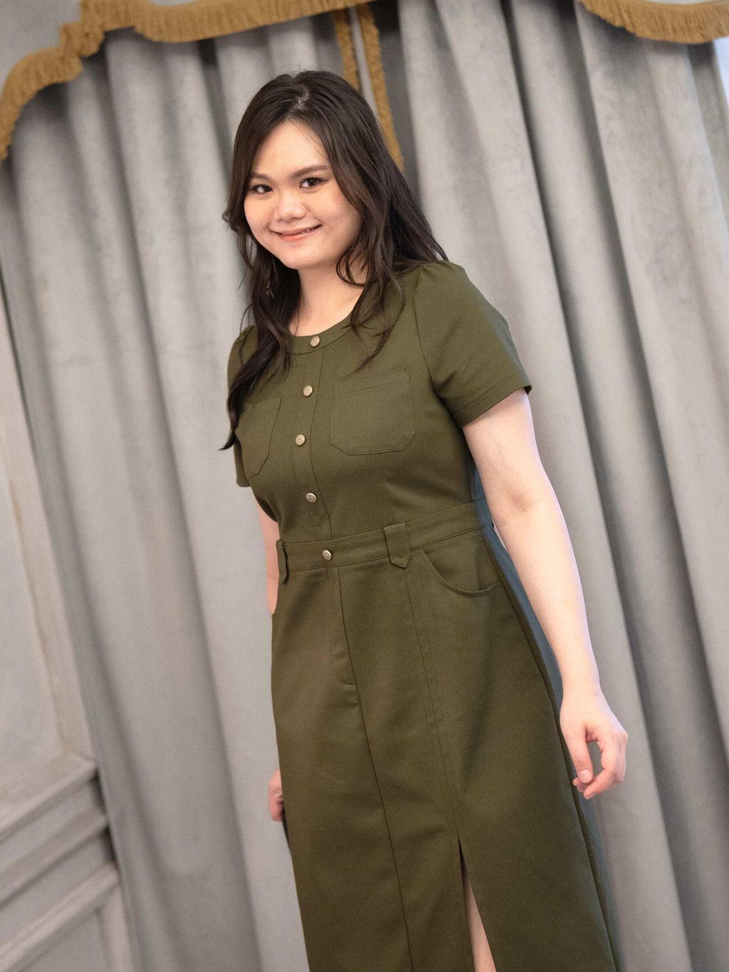 Plus-size model wearing structured army green dress with front slit and flap pockets.