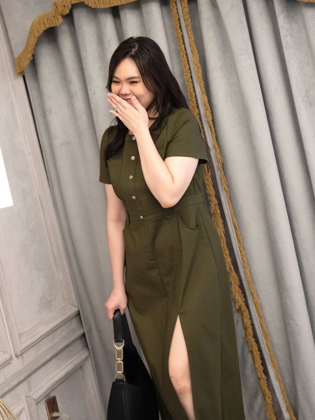 Cheerful plus-size model laughing while wearing an army green dress with a front slit and flap pockets.