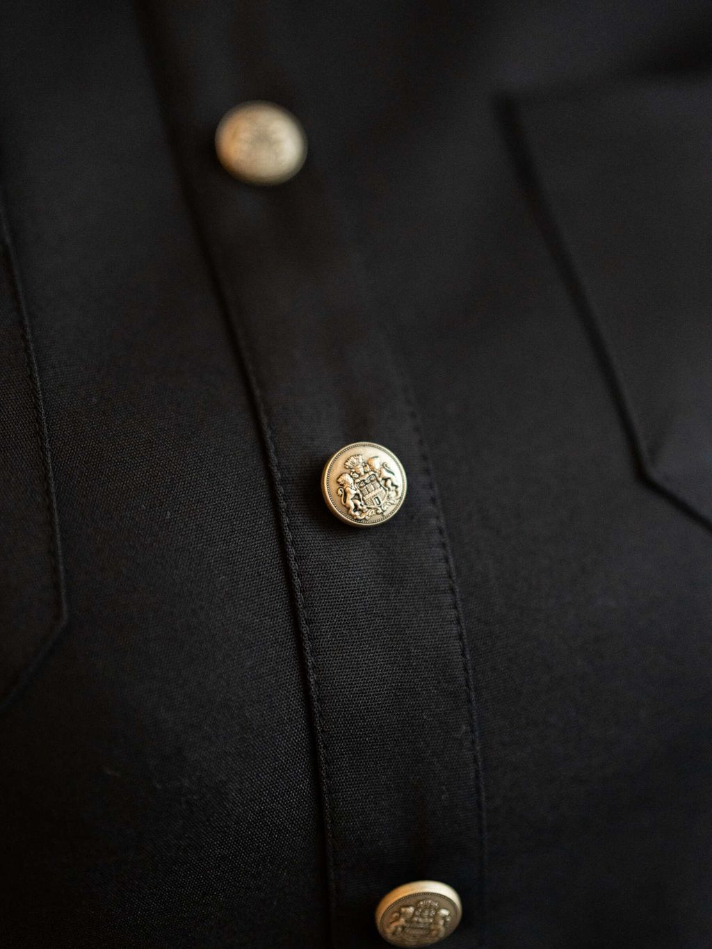 Zoomed detail of crest-style gold buttons on structured black dress.