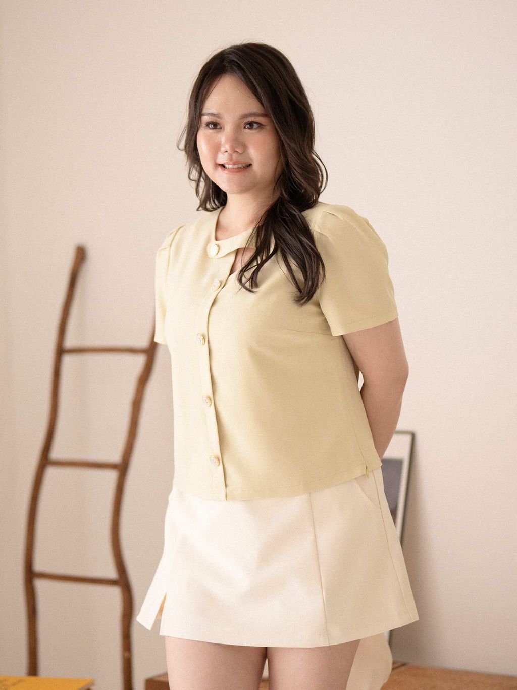 Model smiling in cream skort with front slit, styled with a yellow button-up blouse.