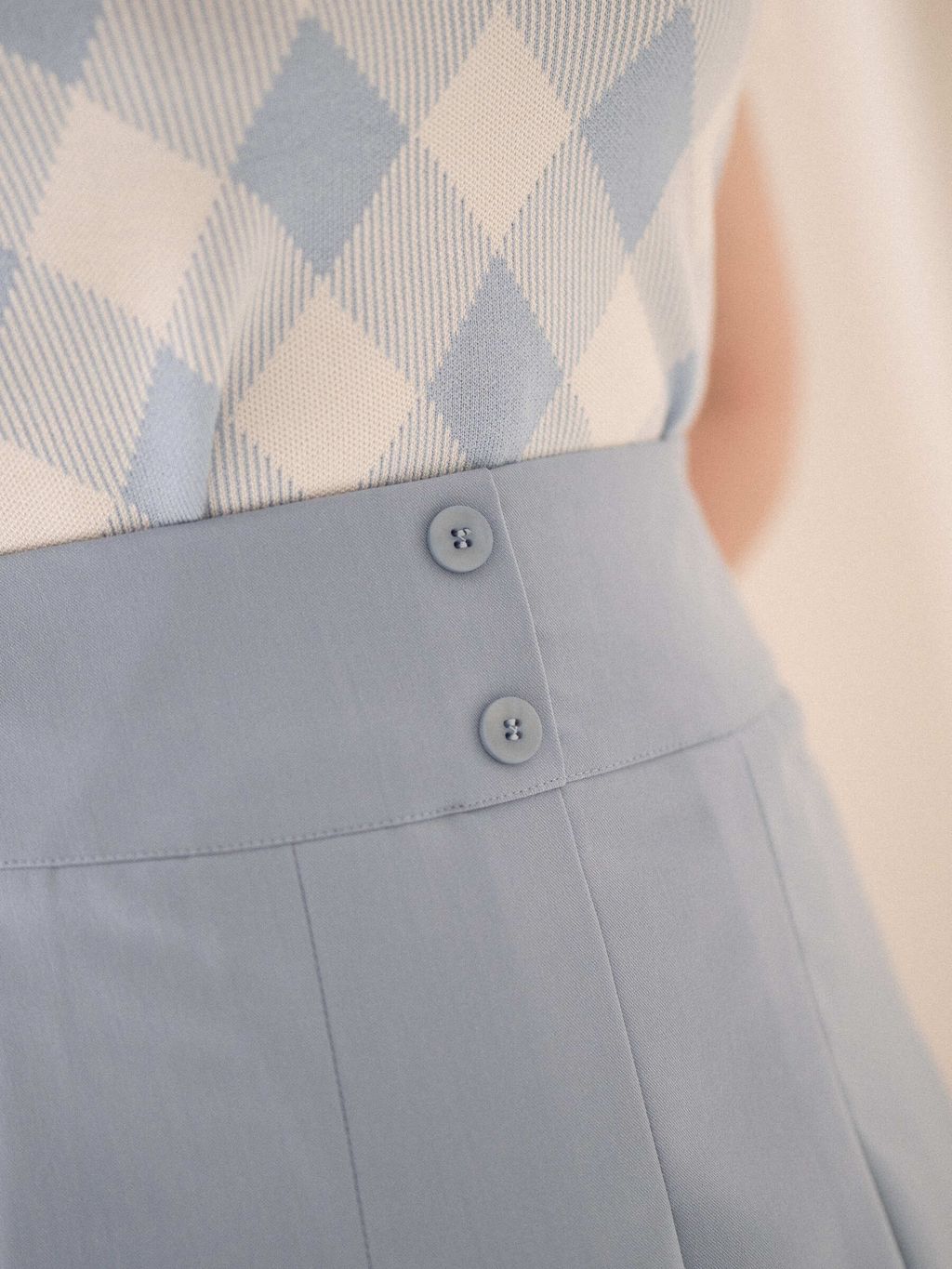 Close-up of blue pleated skirt’s waistband with button details