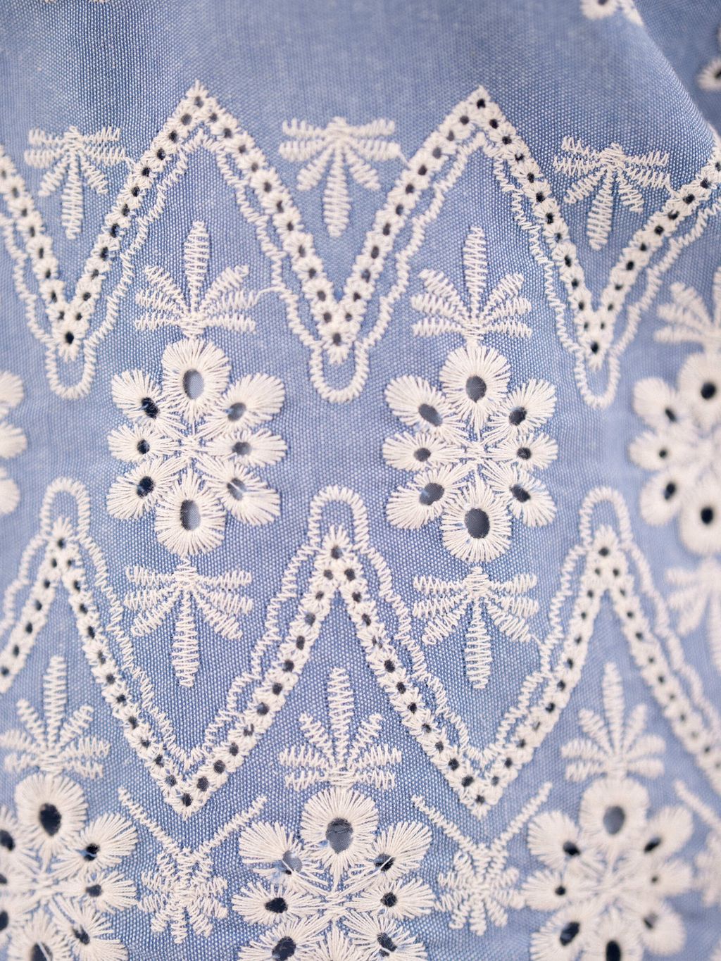 Detailed embroidery of the white floral pattern on light blue fabric