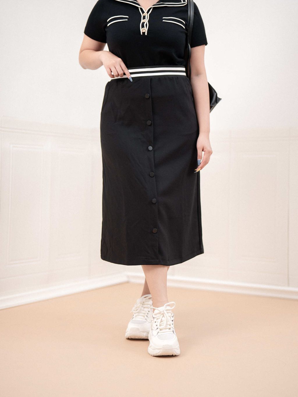 Front view of black A-line midi skirt styled with sneakers