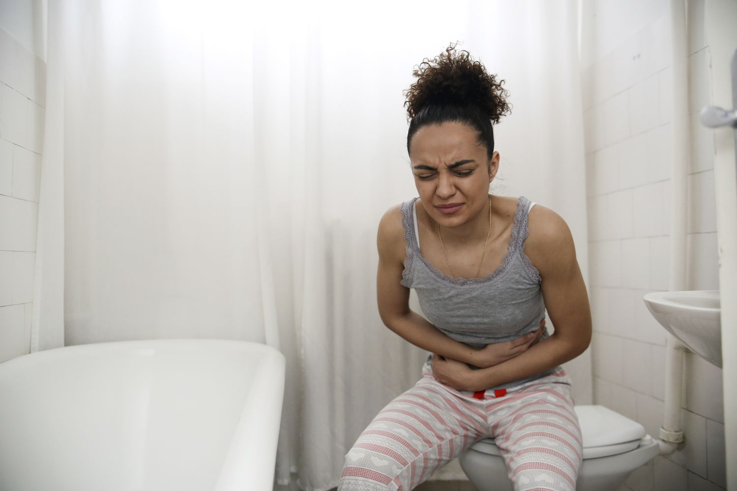 Image showing a lady sitting on a toilet bowl in gray singlet, having constipation and hard to defecate.