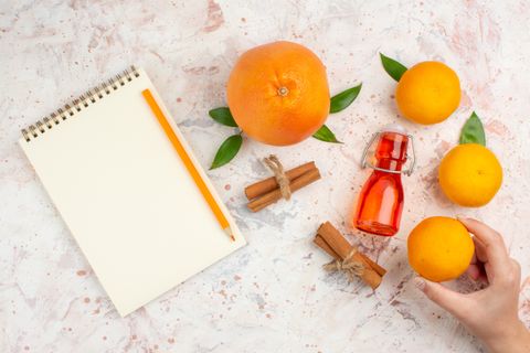 top-view-fresh-orange-cinnamon-sticks-mandarine-female-hand-pencil-notebook-bright-surface