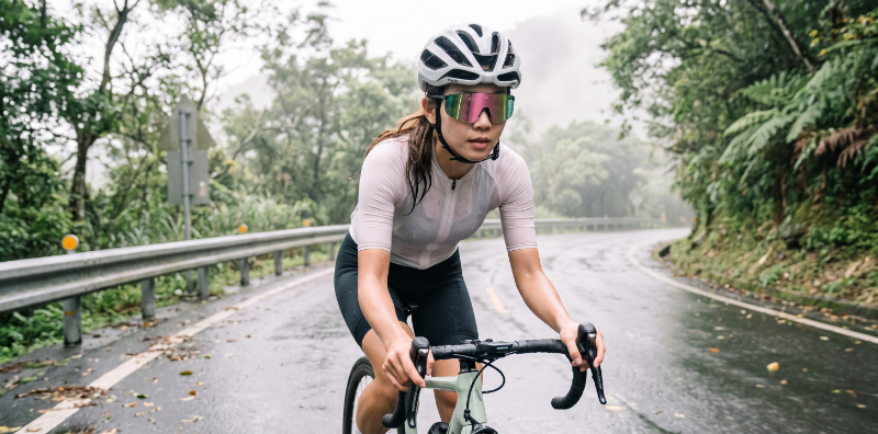 一名台灣自行車手在潮濕的山路上騎行，臉上可見微汗，佩戴 KAKU AIR 運動太陽眼鏡，鏡片依然清晰無霧，展現其在惡劣環境下的卓越耐用性