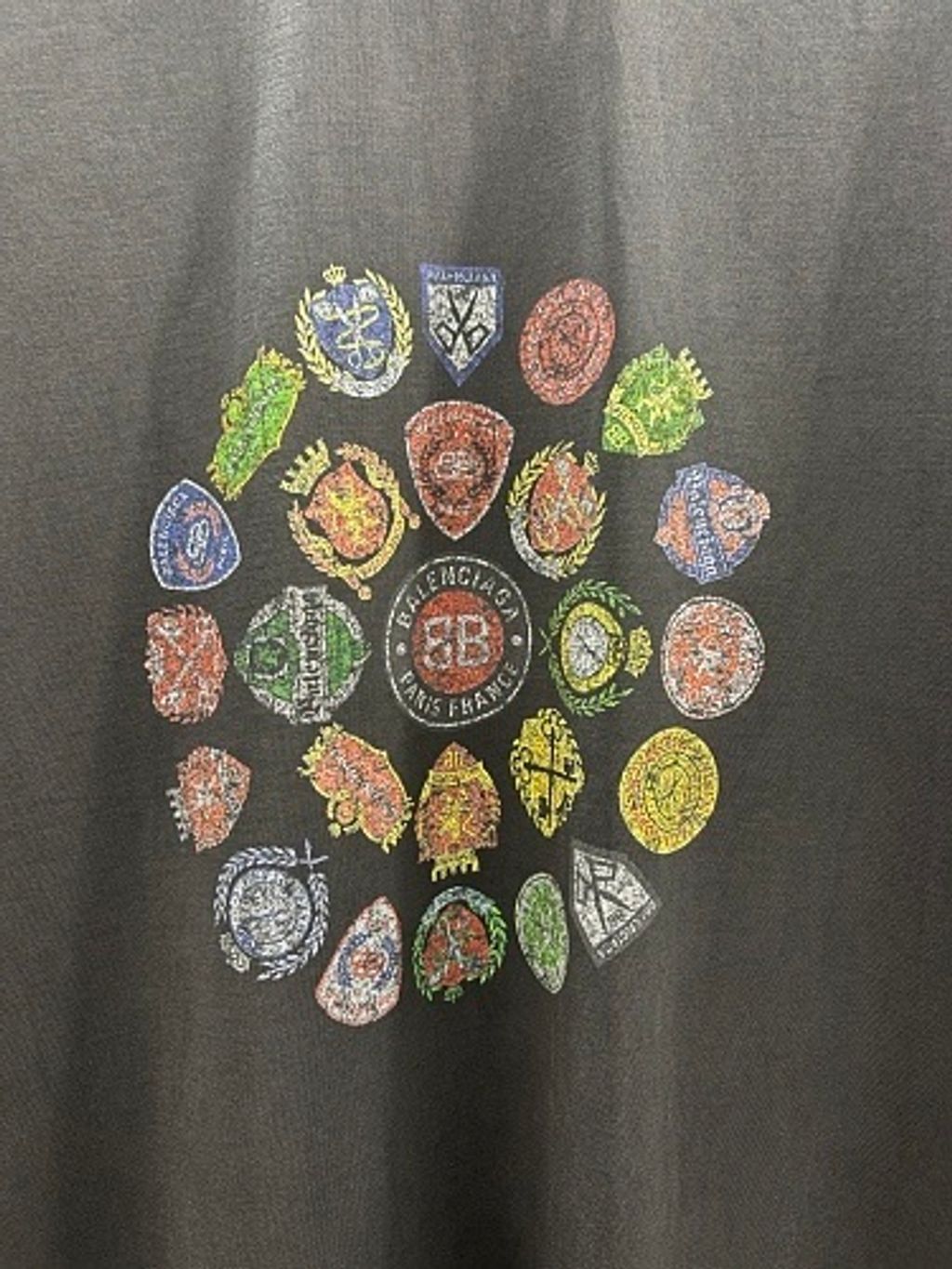 Front and back view of the Balenciaga Vintage Badge Print T-Shirt in washed black, featuring a circular vintage badge graphic on the front, a gothic logo on the back, and a relaxed oversized fit. Available in Singapore and Malaysia.