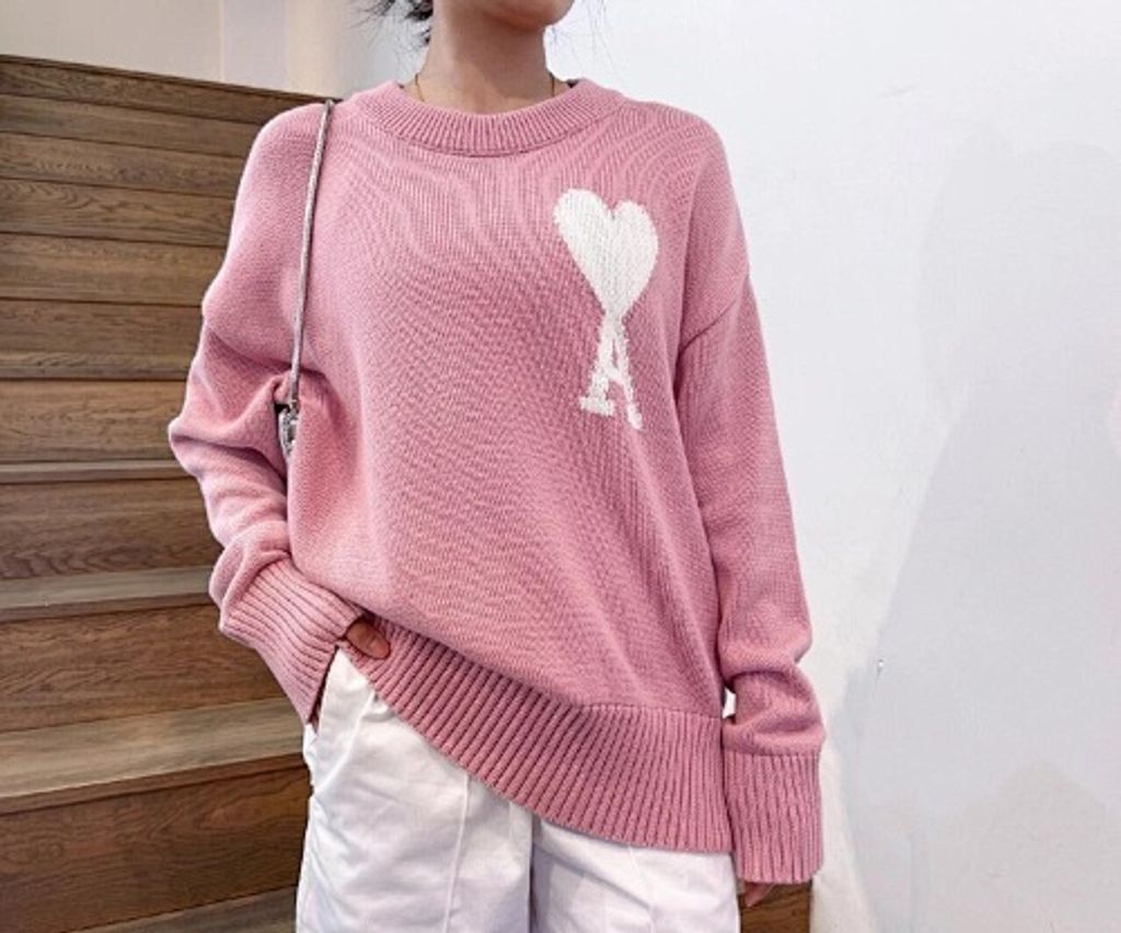 Front and back view of the AMI Paris Ami de Coeur intarsia crewneck sweater in soft pink, featuring a large white knitted "A" heart logo on the chest and a relaxed drop-shoulder fit. Available in Singapore and Malaysia.