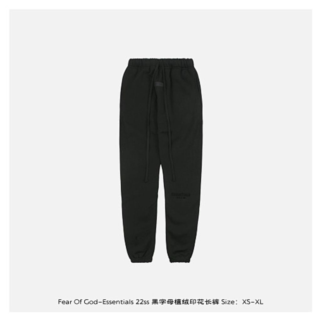 Front and back view of the black Fear of God Essentials sweatpants, featuring a tonal black flocked logo on the left leg, elongated cotton drawstrings, and a relaxed tapered fit. Available in Singapore and Malaysia.