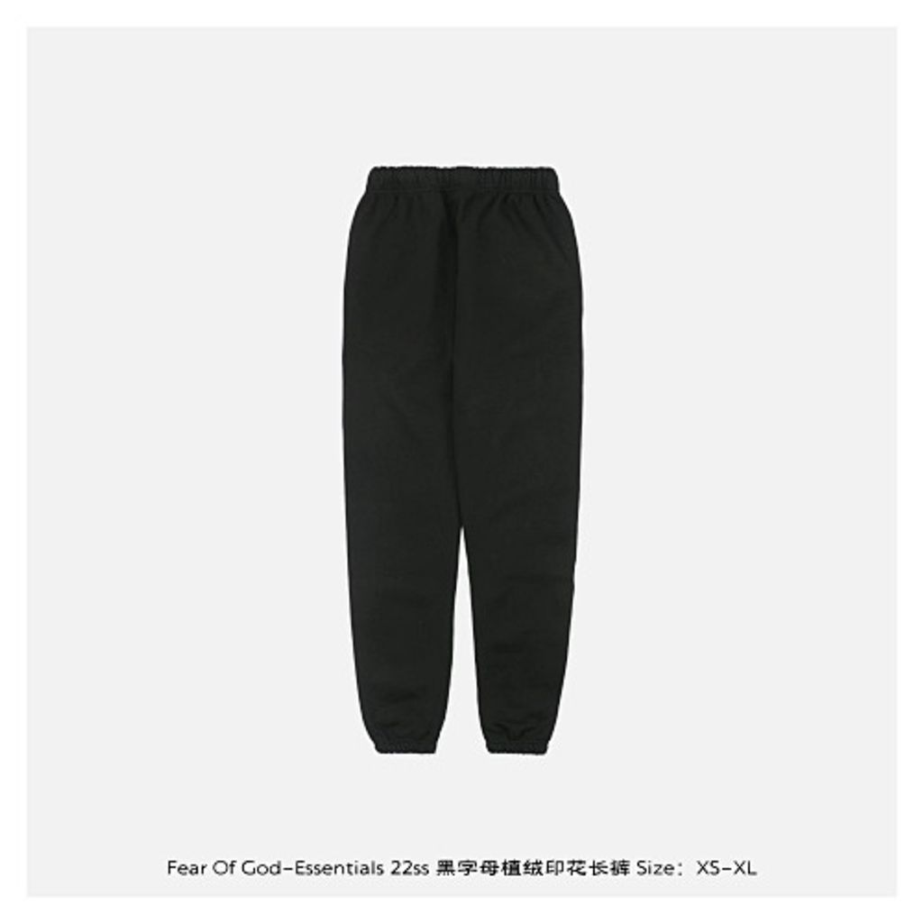 Front and back view of the black Fear of God Essentials sweatpants, featuring a tonal black flocked logo on the left leg, elongated cotton drawstrings, and a relaxed tapered fit. Available in Singapore and Malaysia.