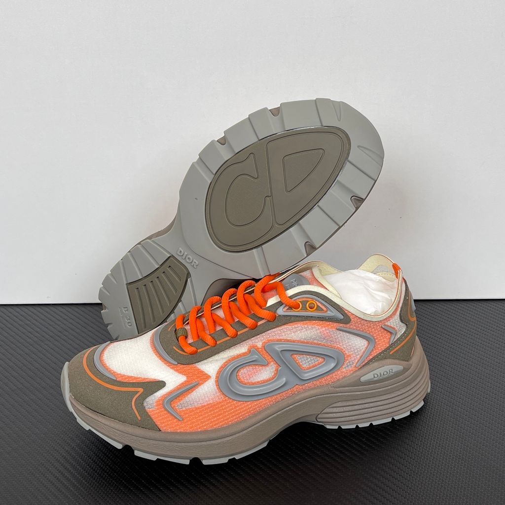 Side profile of the 26SS Dior B30 sneaker in orange and grey, featuring breathable technical mesh, reflective rubber CD30 signatures, and a sculpted lightweight rubber and EVA outsole. Available in Singapore and Malaysia.