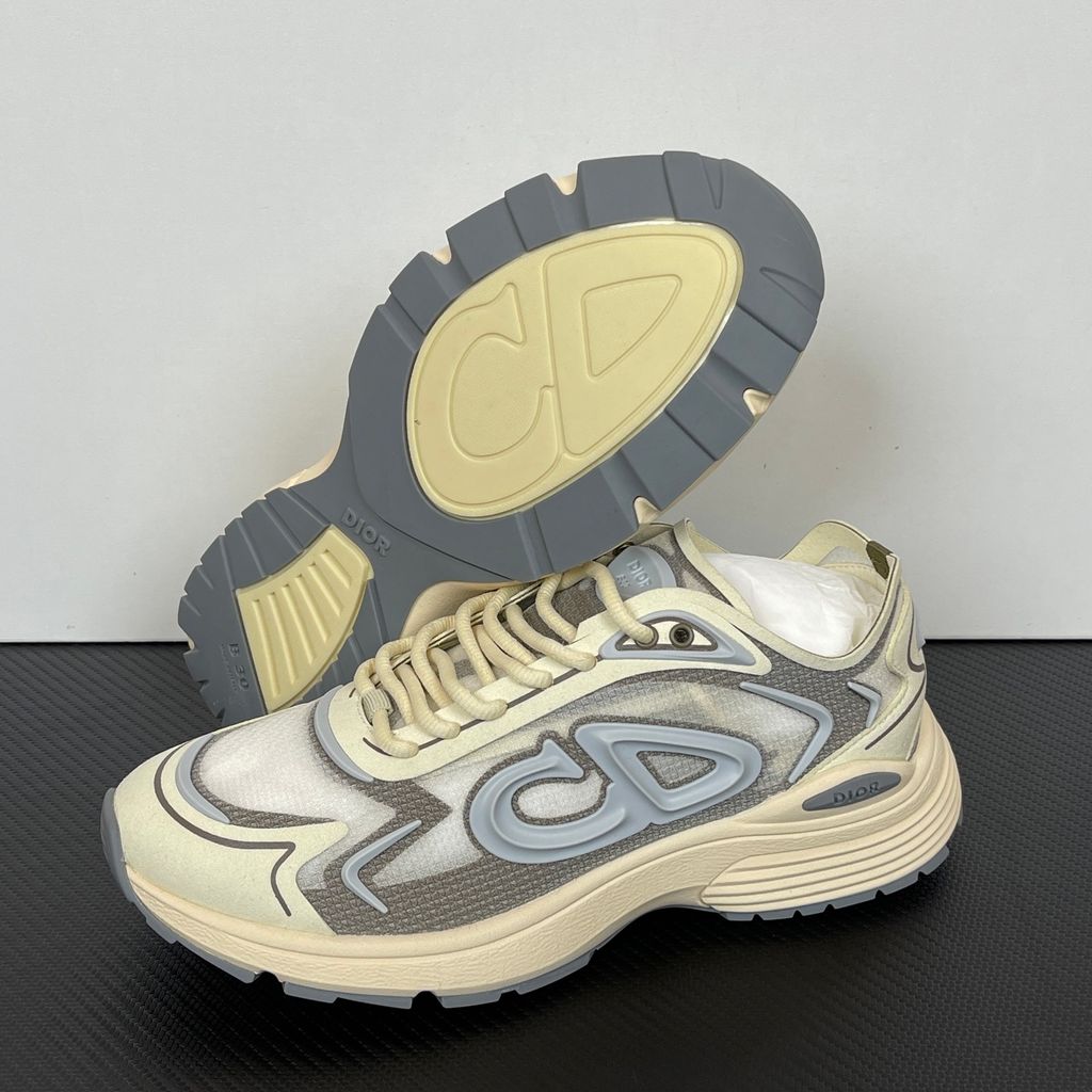 Side profile of the 26SS Dior B30 sneaker in orange and grey, featuring breathable technical mesh, reflective rubber CD30 signatures, and a sculpted lightweight rubber and EVA outsole. Available in Singapore and Malaysia.