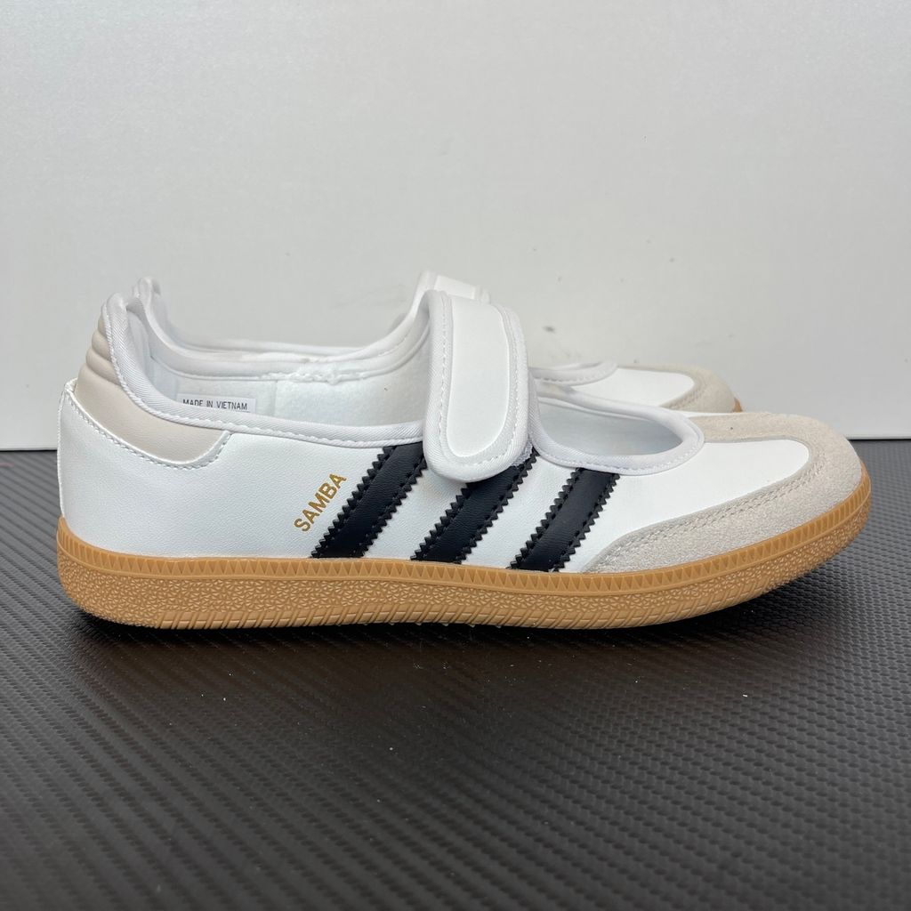 Side profile of the adidas Samba Jane White Black Gum Women's sneaker JR1402, featuring a crisp white leather upper, black serrated 3-Stripes, an adjustable midfoot strap, and a classic gum rubber outsole. Available in Singapore and Malaysia.